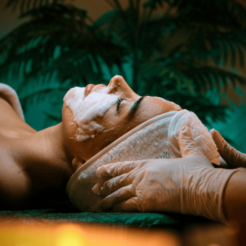 Woman receiving luxury facial treatment at spa with cleansing foam and therapist hands supporting head