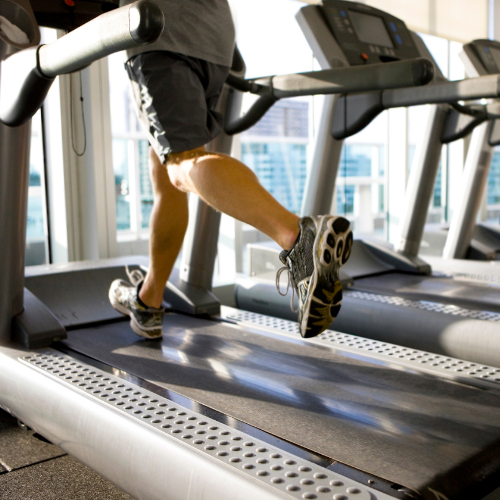 Person running on a treadmill in a modern gym with cardio equipment and city views