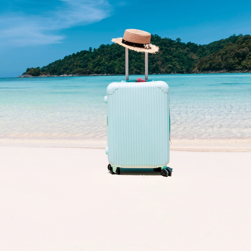 Suitcase with a sun hat on a tropical beach, symbolizing travel and vacation