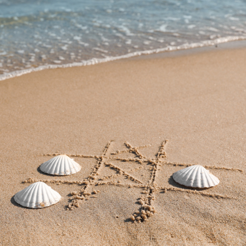 Tic tac toe drawn in sand with seashells on a beach